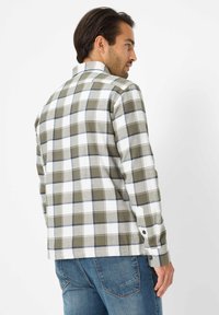 Camicia a quadri verde e bianca con accenti blu, polsini con bottoni e colletto classico, realizzata in un tessuto testurizzato. Indossata con jeans blu.