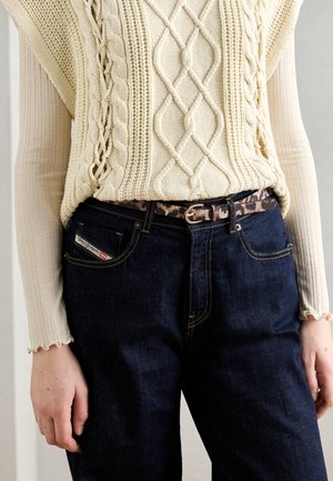Vä beige kabelstickad tröja, mörkblå denimjeans och ett leopardmönstrat bälte. Släta texturer med intrikata stickningar och kontrasterande mönster.