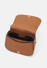 Ruskea nahkainen olkalaukku, jossa on kultaiset yksityiskohdat. Auki oleva läppä paljastaa mustan kankaisen sisustan ja tuotemerkin etiketin sisätaskussa.