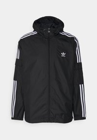 Svart Adidas-jacka med vita tre ränder på ärmarna, huva, framdragkedja och Adidas-logotyp på vänster bröst.
