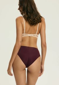 Beżowy biustonosz z koronkowym tyłem i regulowanymi ramiączkami, zestawiony z majtkami w wysokim stanie w kolorze bordowym, o gładkiej fakturze i klasycznym kroju.