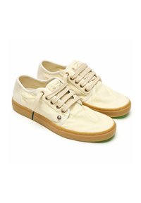 Zapatillas de lona beige con cordones redondos, ojales de metal y suela de goma; textura suave con un branding mínimo.