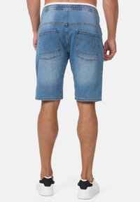 Shorts en denim bleu clair avec taille élastique, deux poches arrière et détails cousus sur l'ourlet. Coupe décontractée et style arrivant au genou.