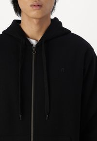 Zwarte zip-up hoodie van een katoenmix, met een capuchon met trekkoord, Zijzakken en een klein logo op de borst.