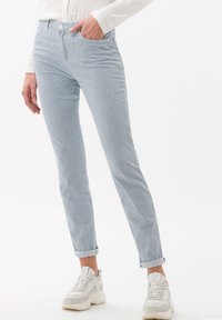 Světle modré kordové kalhoty se slim fit střihem, ohnutými lemy, předními kapsami a jemnou vertikální ribovanou texturou. Vzájemně sladěné s bílými teniskami.