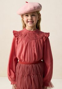 Blouse longue à manches longues rose rosé avec empiècement brodé et épaules à volants, associée à une jupe en tulle à plusieurs couches et un béret rose doux.