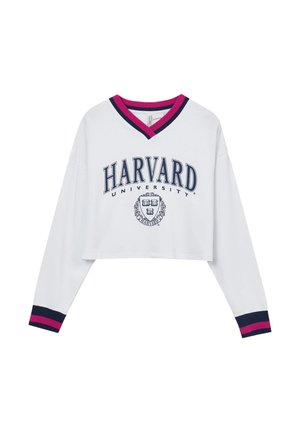 Felpa bianca corta con maniche lunghe, dotata di un colletto a V in rosa e blu navy. Sul fronte c'è la scritta "HARVARD UNIVERSITY" e l'emblema in blu navy.