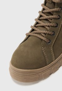 Khaki botki do kostki o zamszowej fakturze, okrągłym nosku i okrągłych, plecionych sznurowadłach. Wzmocnione szwy oraz gumowa podeszwa z poziomymi rowkami.