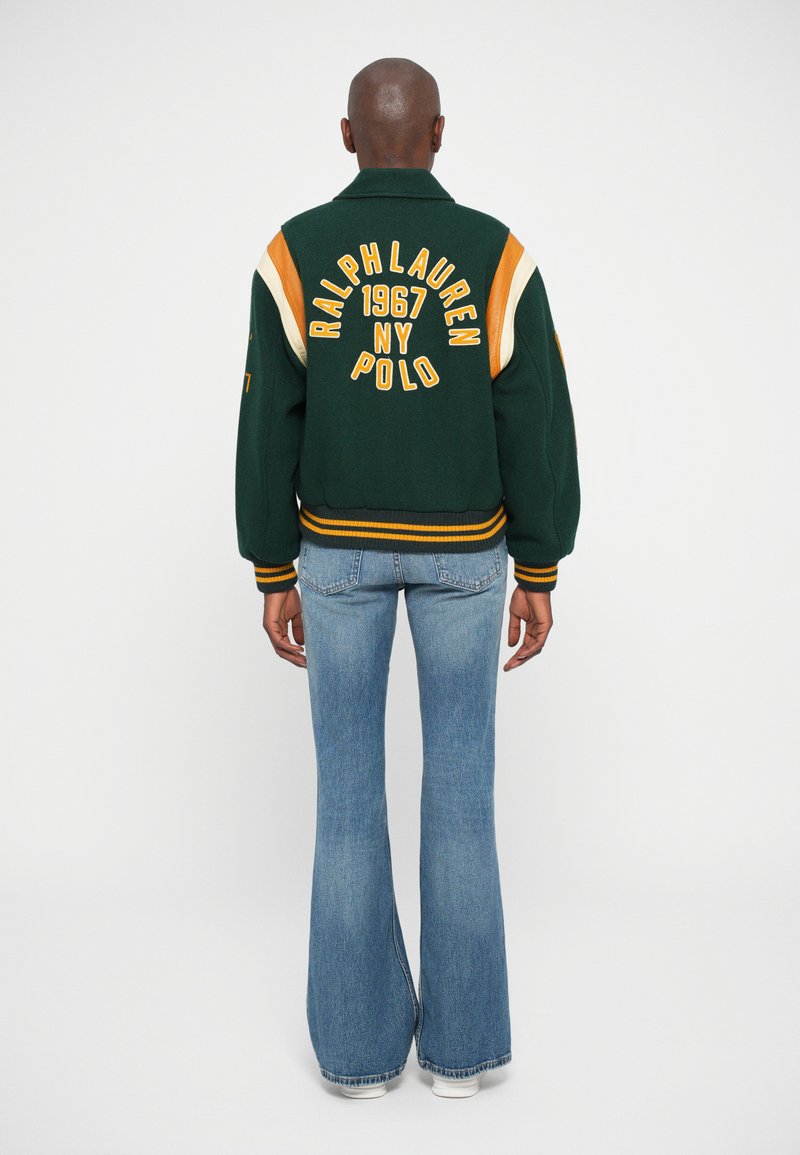 Zaļa vilnas maisījuma varsity jaka ar oranžiem un krēmkrāsas akcentiem, uz muguras ar izšuvumu "RALPH LAUREN 1967 NY POLO", ribotas aproces.