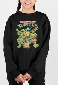 Sort sweatshirt med en farverig tegneserie grafik af fire skildpadder, i grønne og brune farver, og en hyggelig, blød tekstur.