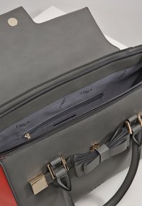 Szara torebka z sztucznej skóry, ozdobiona kokardą, z złotymi akcentami i teksturowanym wykończeniem; wnętrze wykończone gładką, szaro-skalną podszewką oraz kieszonką na zamek.