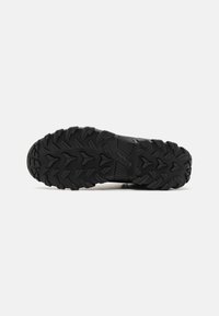 Semelle extérieure en caoutchouc noir avec des crampons profonds, présentant une surface texturée et des rainures angulaires pour l'adhérence. Durable et conçu pour une utilisation en extérieur.