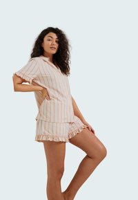 Ensemble de pyjama léger à rayures dans des teintes pastel de rose et de crème ; comprend un haut à manches courtes avec boutons et un short à volants. Texture de tissu douce.