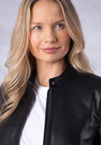 Black leather jacket with a stand collar and a zipper closure. Worn over a plain white shirt, featuring smooth texture and subtle sheen.