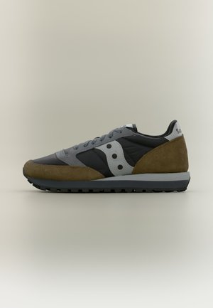 Baskets à profil bas avec des panneaux en suède noir, gris et marron, comportant un logo blanc sur le côté et une semelle en caoutchouc noire texturée.