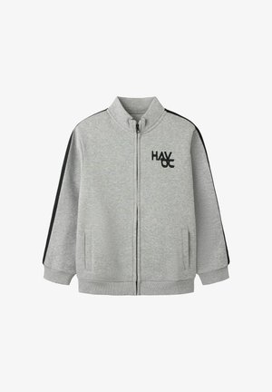 Sweat-shirt zippé gris clair avec des bandes noires sur les manches et un logo "HAV OC" noir sur la poitrine gauche, avec un col montant et des poches latérales.