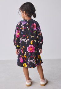 Mustast lillemustrist kleit, millel on erksavärvilised mitmevärvilised lilled, pikad varrukad ja kootud seelik. Tagaküljel nööpidega sulgur. Valgete ja tan värvi tossudega kokku sobitatud.