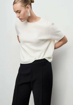 Haut blanc texturé à manches courtes associé à un pantalon noir ajusté. D'étonnantes boucles d'oreilles transparentes complètent le design minimal de la tenue.