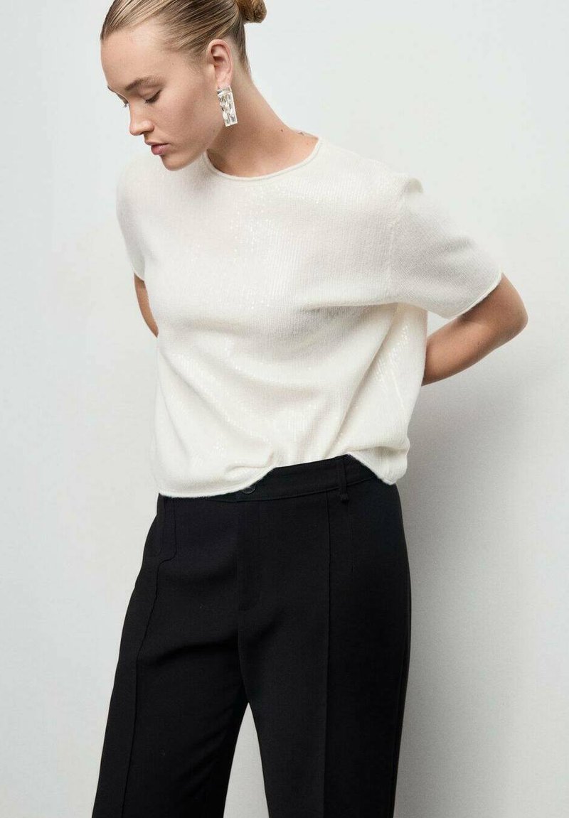 Top blanco texturizado con mangas cortas, combinado con pantalones negros a medida. Pendientes claros destacados complementar el diseño minimalista del atuendo.