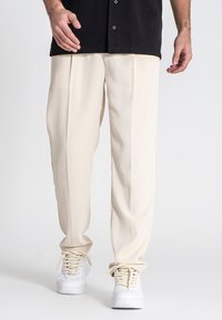 Cremefarvede bukser med løs pasform, der har to forskydninger foran, blød tekstur og lige ben, parret med hvide sneakers.