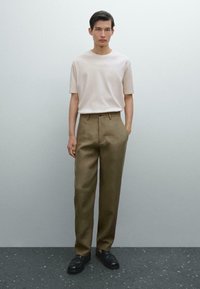 Maglietta beige a maniche corte abbinata a pantaloni a vita alta verde oliva. Scarpe nere completano l'outfit. Texture lisce, design minimale.