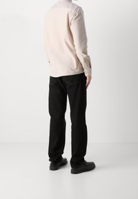 Lichtgekleurde overhemd met lange mouwen, gecombineerd met zwarte broek en donkere schoenen. Fijne stof met een ontspannen pasvorm.