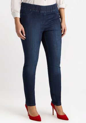 Jeggings de color azul oscuro con cintura elástica, bolsillos frontales, un ajuste slim y textura de denim suave, combinados con zapatos de tacón alto rojos.