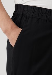 Černé šortky s elastickým pasem a bočními kapsami, vyrobené z hladkého a lehkého materiálu, s elegantním a přiléhavým střihem.