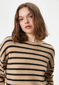 Maglione beige con strisce orizzontali nere, texture morbida, scollatura a girocollo e spalle scese, con una vestibilità rilassata.