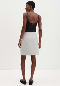 Zwarte rugloze tanktop, grijze wolmix A-lijn rok en zwarte platte schoenen met studs, met gladde texturen en strakke lijnen.
