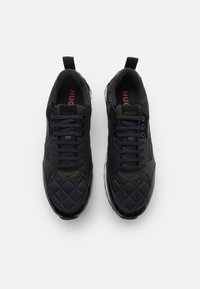 Czarne trampki z pikowaną fakturą, wyposażone w sznurowanie, gumowe podeszwy oraz kontrastującą białą podeszwę zewnętrzną. W środku na czerwono nadrukowano napis "Hugo".