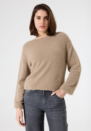 Pull en fausse fourrure beige avec un col rond et des manches longues, associé à un jean gris foncé. Le pull présente une surface douce et texturée.