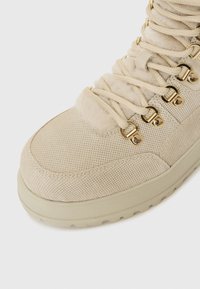 Baskets montantes beiges avec une texture en daim, panneaux en maille et œillets dorés. Les lacets sont noués de manière classique, mettant en valeur une doublure douce et duveteuse.