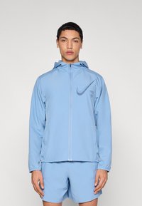 Μπλε ελαφρύ μπουφάν με φερμουάρ και κουκούλα, με λογότυπο Nike σε πιο σκούρο μπλε, κατασκευασμένο από λείο, αναπνέον ύφασμα.
