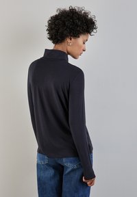 Långärmad marinblå topp med ståkrage, tillverkad av mjukt tyg, med en smal passform och diskreta sidoklipp, i kombination med ljusblå jeans.