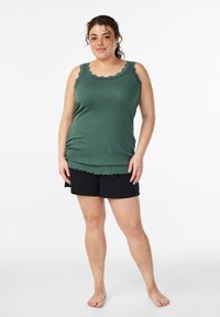 Dunkelgrünes Tanktop mit gewelltem Spitzenkragen, kombiniert mit schwarzen Shorts. Weiche Textur, lockere Passform und keine sichtbaren Muster oder Verzierungen.