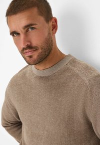 Light brown knitted sweater with a textured appearance, featuring a round neckline and subtle ribbed detailing on the sleeves.