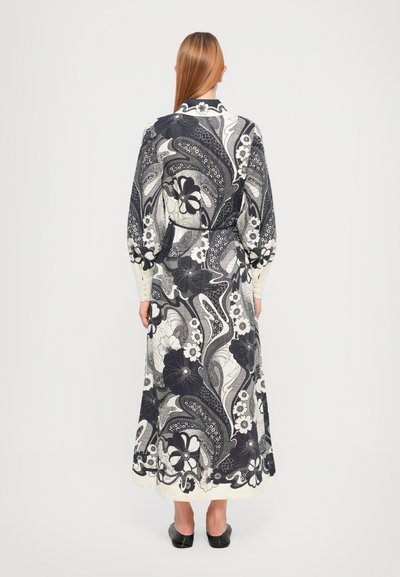 Vestido largo y estampado que presenta un diseño floral en blanco y negro, con mangas largas y un cinturón en la cintura, terminado con una textura de tela ligera.