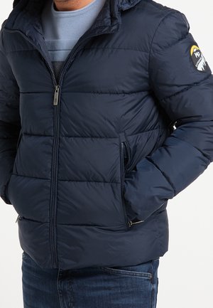 Marineblauwe pufferjack gemaakt van nylon, met gestikte delen, een ritssluiting aan de voorkant, zijzakken en een logopatch op de linkermouw.