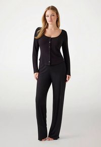 Mustast pehmest kangast pikkade varrukatega ümar kaelusega ja nööpidega top, mis on kombineeritud lahtiste mustade pükstega.