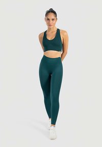 Turquoise geribbelde sportbeha met bijpassende, hoge taille sportlegging, gemaakt van rekbare stof, gecombineerd met witte sneakers. Minimalistisch ontwerp, naadloze randen.