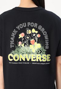 Black cotton t-shirt featuring colorful floral graphic with text "THANK YOU FOR GROWING" and brand name "CONVERSE" in white and green.