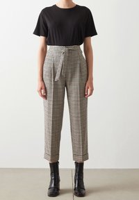 Černé tričko s krátkým rukávem v kombinaci s vysokými kostkovanými kalhotami se páskem, udržující strukturovaný střih, a černé boty po kotníky.