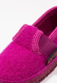Vilt slippers in een levendig roze met een gestructureerde afwerking, voorzien van een brede stofband en contrasterende stiksels langs de randen.