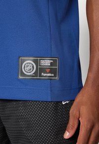 Blå sportsdrakt med strukturert stoff; har NHL- og Fanatics-logoer; kombinert med svarte mesh-shorts med hvite prikker.