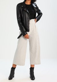 Black leather motorcycle jacket over a black top, paired with high-waisted striped wide-leg pants and black ankle boots.