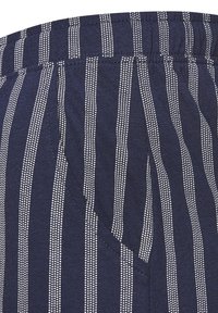 Navy blue fabric with white vertical stripes, featuring a relaxed waistband and side pocket, made of soft cotton blend material.