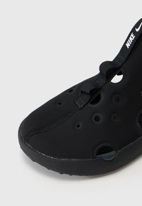 Černá slip-on bota s texturovaným, perforovaným designem. Disponuje flexibilním tělem a kontrastním pásem přes svršek pro bezpečné upevnění.