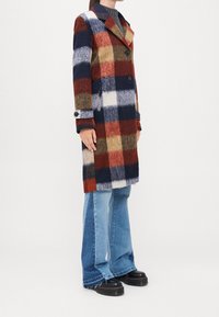 Cappotto in misto lana con un motivo a quadri multicolore in rosso, blu navy e crema. Presenta un ampio colletto, due bottoni e una vestibilità slim.