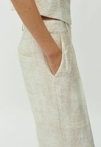 Lichtbeige broek met een subtiele textuur, voorzien van zijzakken, een ontspannen pasvorm en een soepele tailleband. Minimalistisch ontwerp met een gedempt patroon.